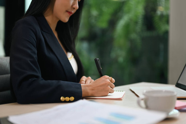 Professional millennial businesswoman sitting at her workplace and signing document. - 写真・画像