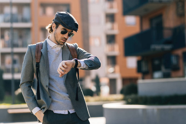 Young businessman standing on the street and looking at time on his wristwatch.  - Foto, immagini