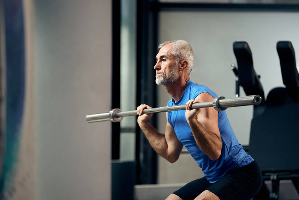 Mature athletic man lifts barbell while exercising strength in g - Foto, imagen