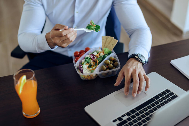 Unrecognizable businessman eating healthy food and surfing the net on laptop on lunch break in the office.  - Photo, Image