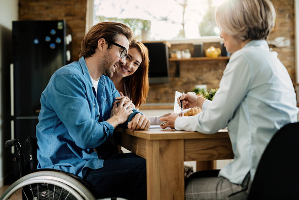 Young happy couple and their financial advisor using touchpad on a meeting at home. Focus is on man in wheelchair.  - Fotoğraf, Görsel