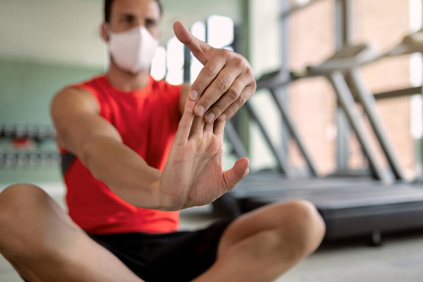 Close-up of athletic man with protective face mask warming up and stretching his arms in health club.  - Foto, immagini