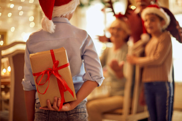 Back view of little boy surprising his family with Christmas gift while celebrating holiday at home. - Foto, Bild