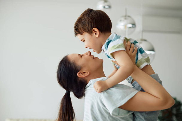 Young playful mother having fun with her small boy at home. Copy space. - 写真・画像