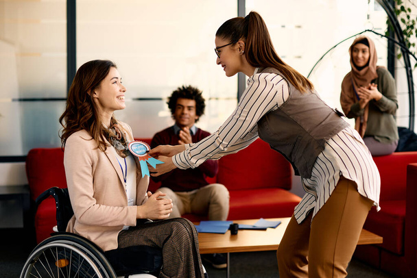 Счастливая деловая женщина в инвалидной коляске получает работника месяца награду ленты от своего коллеги на церемонии в офисе. - Фото, изображение