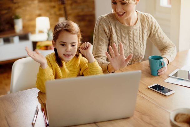 Happy mother and daughter using laptop and waving during video call at home.  - 写真・画像