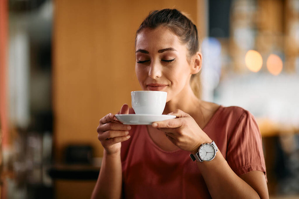 Smiling woman enjoying with eyes closed in cup of fresh coffee at cafe.  - Photo, Image