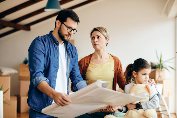Mid adult parents with daughter feeling displeased while analyzing blueprints after moving in a new house.  - Photo, Image
