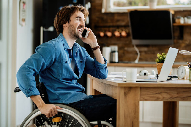 Молодий щасливий бізнесмен в інвалідному візку працює вдома і розмовляє по мобільному телефону
.  - Фото, зображення