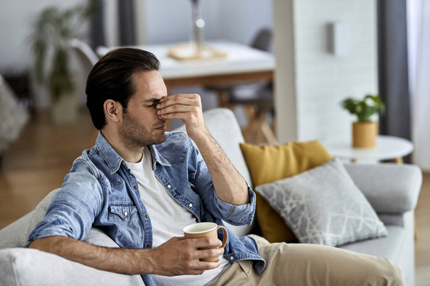 Young man having a headache while drinking coffee in the living room.  - 写真・画像