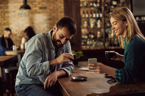 Счастливая пара читает что-то смешное на смартфоне, когда пьет кофе в кафе. - Фото, изображение