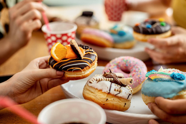 Close-up of unrecognizable people eating glazed doughnuts. - Valokuva, kuva
