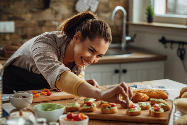 jong gelukkig vrouw genieten terwijl het maken van bruschetta in de keuken.  - Foto, afbeelding