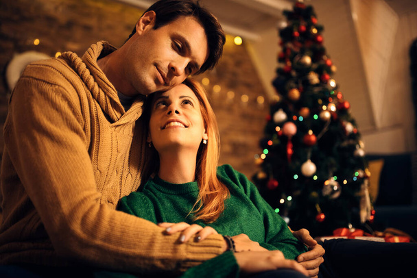 Affectionate couple embracing while relaxing on Christmas eve at home.  - Φωτογραφία, εικόνα