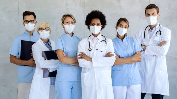 Grupo de trabajadores sanitarios que usan mascarillas protectoras mientras están de pie con los brazos cruzados y mirando a la cámara.  - Foto, imagen