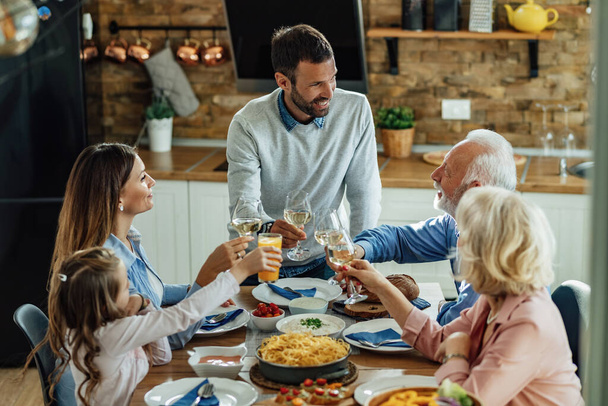 Happy extended family talking while having lunch and toasting at dining table.  - Foto, imagen