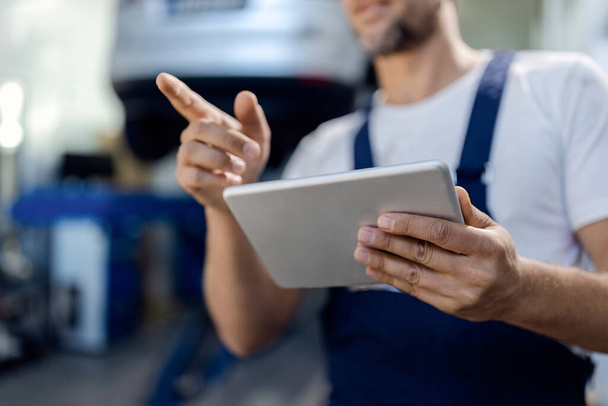 Close-up of auto repairman working on digital tablet in a workshop.  - 写真・画像
