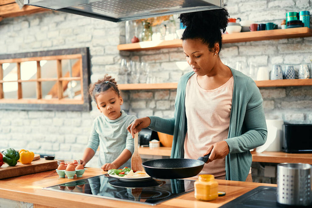 Afro-Amerikaanse moeder en dochter bereiden samen ontbijt in de keuken. - Foto, afbeelding