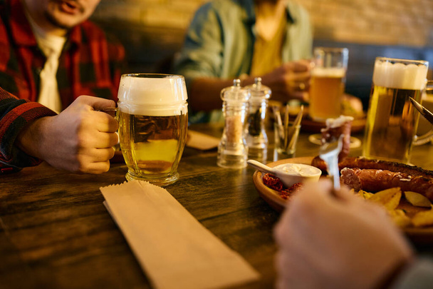 Close-up of male friends enjoying while eating lunch and drinking beer in a pub.  - Foto, imagen