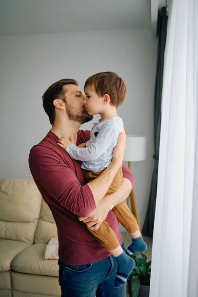 Affectionate father holding his son and kissing him at home. - Valokuva, kuva