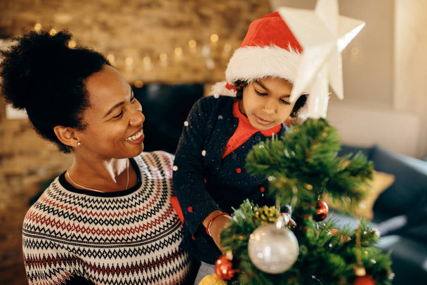 Happy African American äiti ja hänen pieni tyttö valmistautuu loma ja koristelu joulukuusi kotona.  - Valokuva, kuva