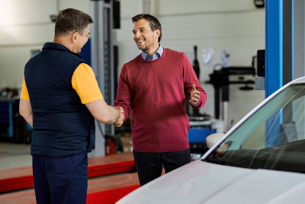 Happy male customer handshaking with a mechanic in auto repair shop.  - Foto, Imagen