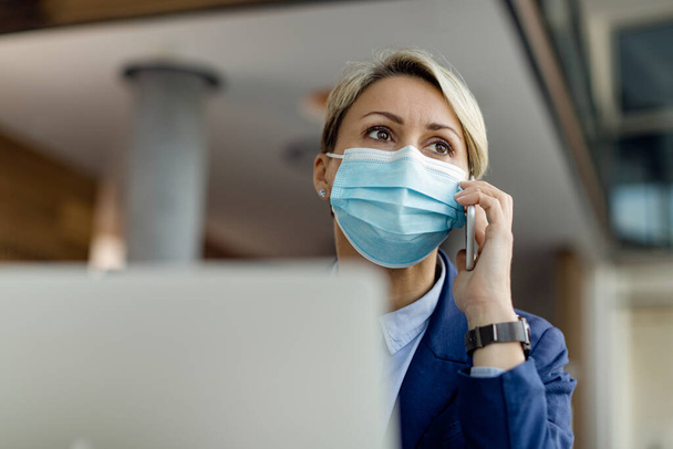 Low angle view of female entrepreneur wearing protective face mask while making a phone call in the office.  - Photo, Image