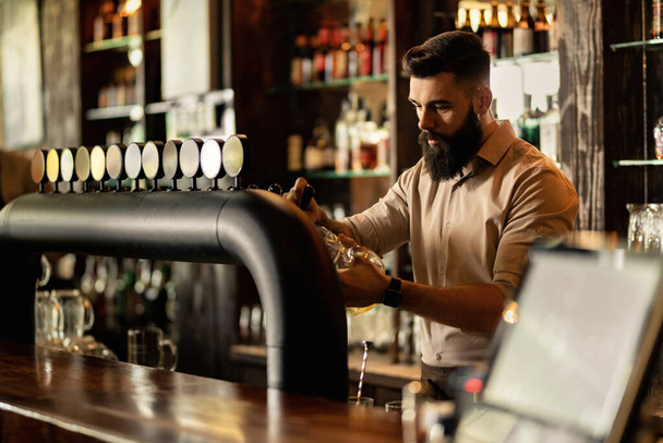 Young bartender working at bar counter and pouring beer in a glass.  - Photo, Image