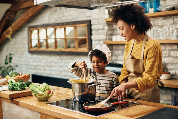 Small black boy preparing food with his mother in the kitchen.  - Valokuva, kuva