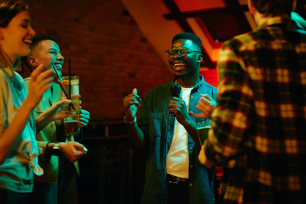 Веселим друзьям веселиться в баре ночью. Фокус на афроамериканця, який підписує караоке..  - Фото, зображення