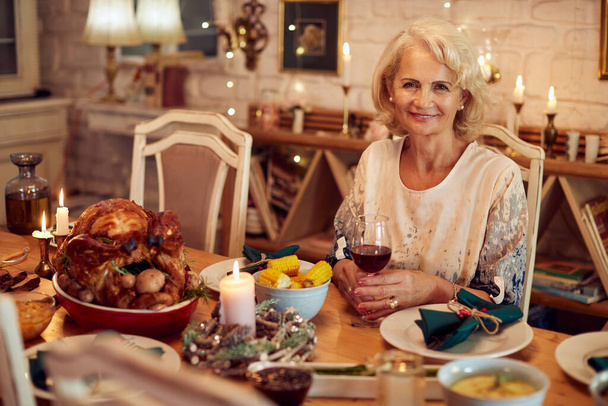 Happy mature woman sitting at dining table on Christmas at looking at camera. - Foto, afbeelding