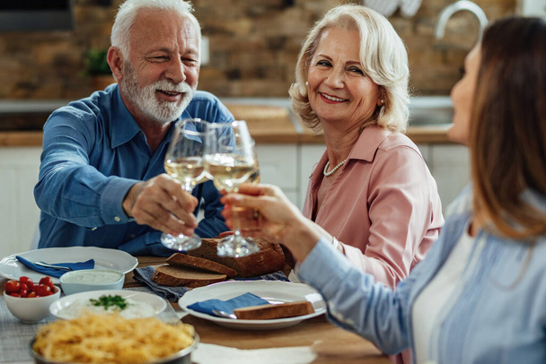 Happy mature parents and their adult daughter toasting with wine during lunch in dining room. Focus is mature woman.  - Φωτογραφία, εικόνα