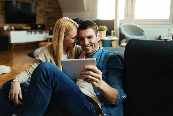 Young happy couple surfing the net on touchpad while relaxing in the living room. - Photo, Image