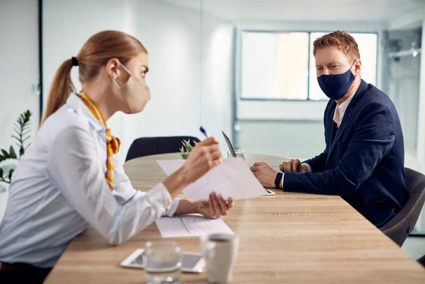 Business colleagues going through paperwork and talking in the office while wearing protective face masks due to coronavirus pandemic.  - Foto, Imagen