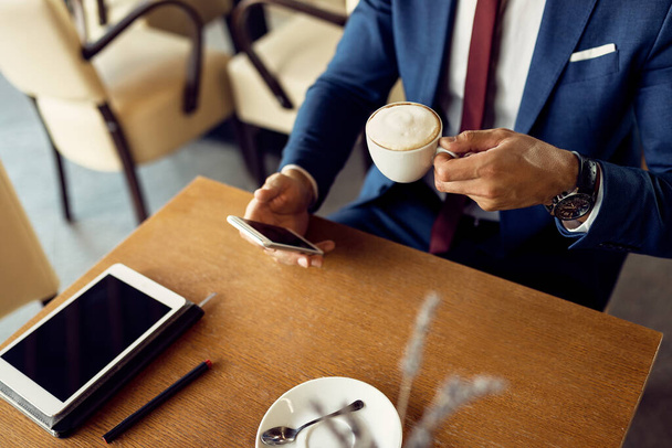 Невпізнаваний бізнесмен п'є каву під час текстових повідомлень на смартфоні і розслабляється в кафе
.  - Фото, зображення