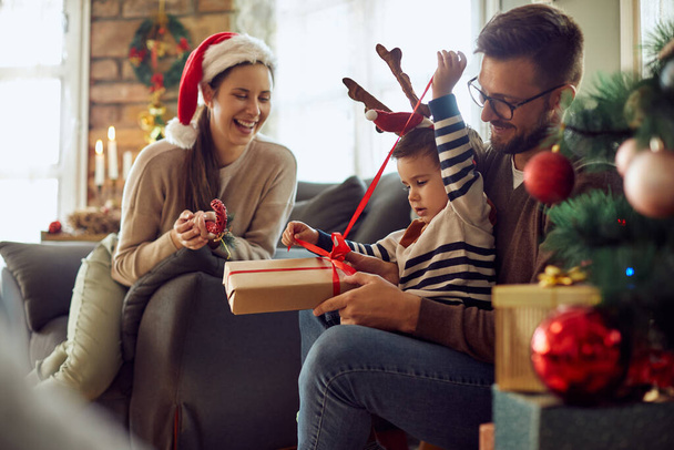 Happy parents and their son having fun while opening Christmas gifts at home. - Photo, image
