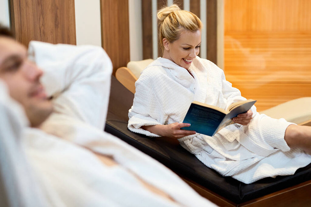 Happy woman relaxing with her husband at the spa and reading a book.  - 写真・画像