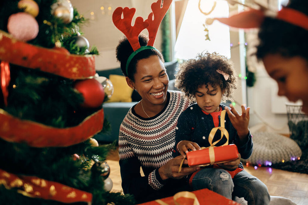 Щаслива чорна мати та її маленька донька відкривають подарунки та розважаються на Різдво вдома
.  - Фото, зображення