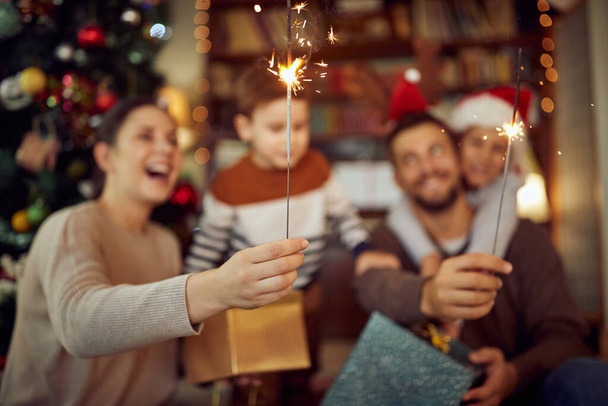 Closeup of family celebrating Christmas and having fun with sparklers at home. - Foto, imagen