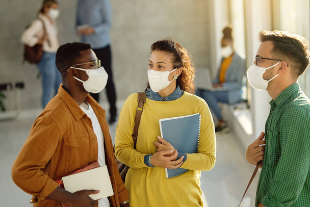 University students wearing protective face masks and communicating while standing in a hallway. Focus is on female student.  - Fotografie, Obrázek