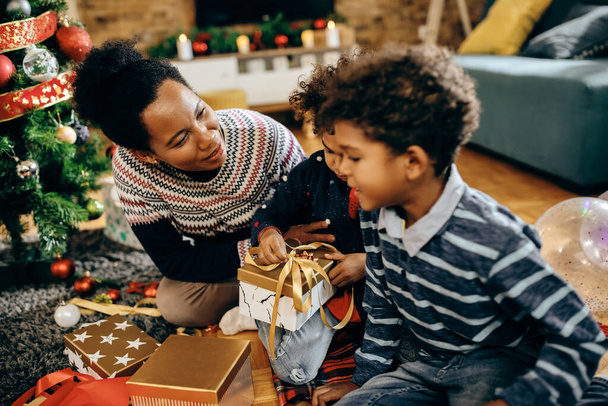 Щаслива чорна мати і діти спілкуються під час розгортання подарунків на Різдво вдома
.  - Фото, зображення