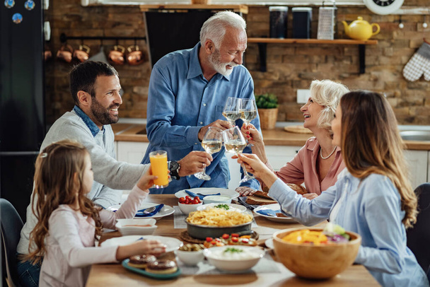 Щаслива розширена сім'я насолоджується обідом і тостами за обіднім столом. Фокус на старшій парі
.  - Фото, зображення