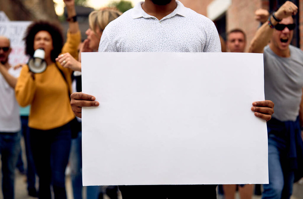 Невпізнаваний чорний чоловік протестує з багатоетнічною групою людей і тримає порожній плакат. Копіювати простір
.  - Фото, зображення