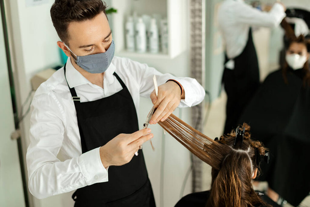 Hairdresser and his customer wearing protective face masks during a haircut at the salon. - Foto, Imagem
