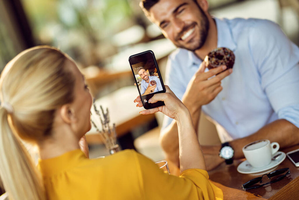 Happy couple having fun while eating donut and taking picture with smart phone. Focus is on man on phone's screen.  - Fotoğraf, Görsel
