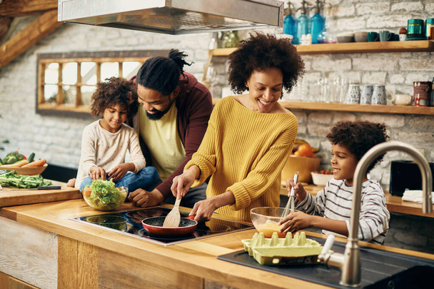 Happy black parents and their kids preparing food in the kitchen. Focus is on mother.  - Fotografie, Obrázek