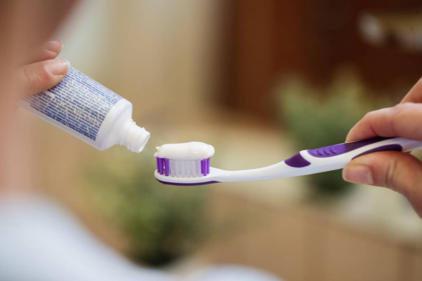 Крупним планом невизначена жінка наносить зубну пасту на зубну щітку у ванній
.  - Фото, зображення