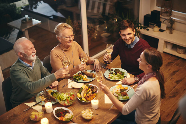 High angle view of happy senior woman toasting with her family while having a meal at dining table.  - Photo, Image