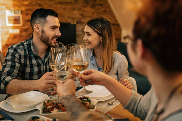 Happy couple looking at each other while toasting with friends during dinner at home.  - Foto, Imagen
