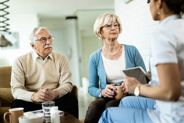 Senior couple talking to healthcare worker during home visit. Focus is on senior woman.  - 写真・画像